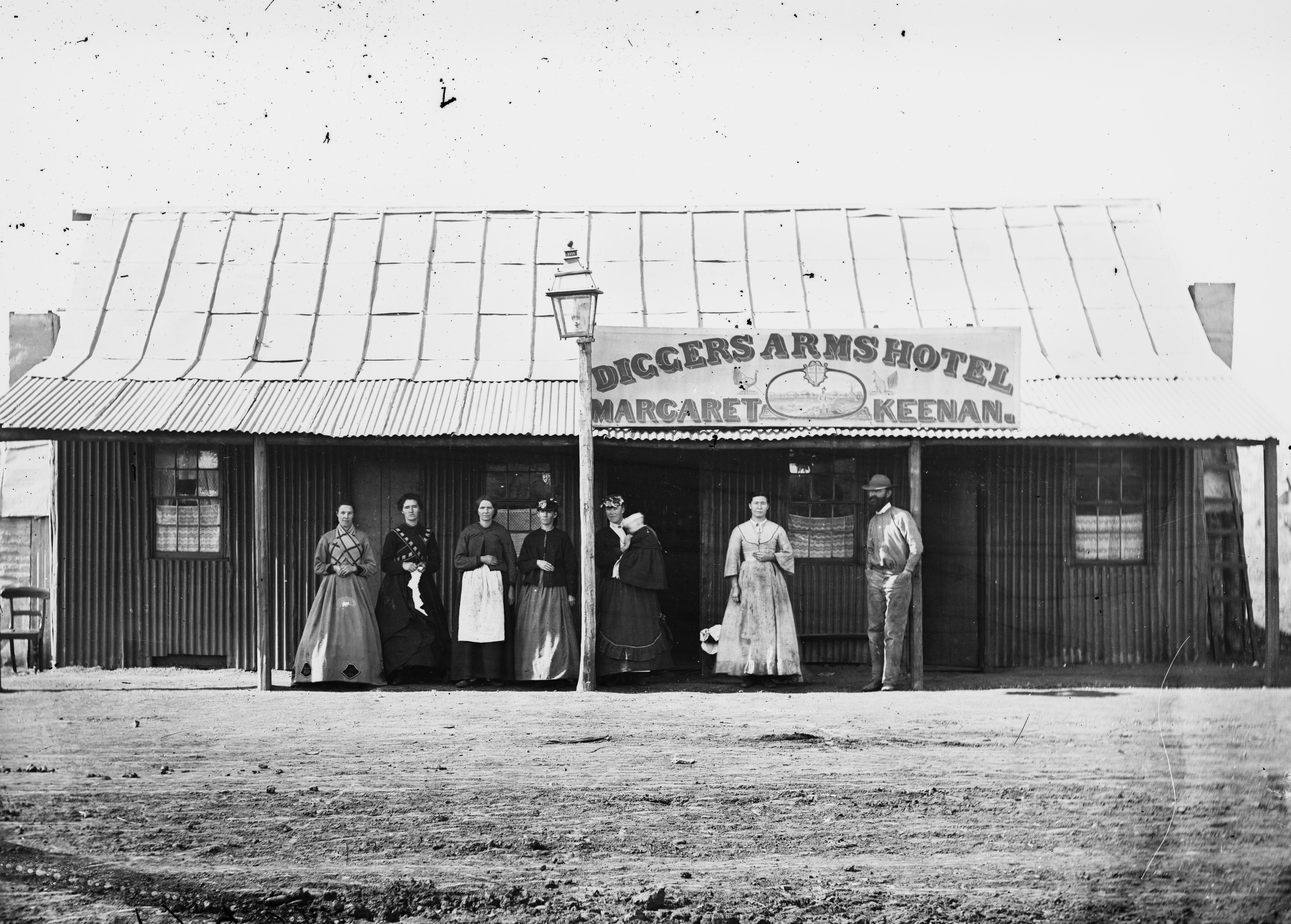 An 1800s black and white photo of a pub called the Diggers Arms Hotel, with a group of women and a man