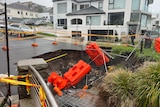 A sinkhole emerging in an affluent Sydney suburb, near the ocean, with rainclouds overhead.