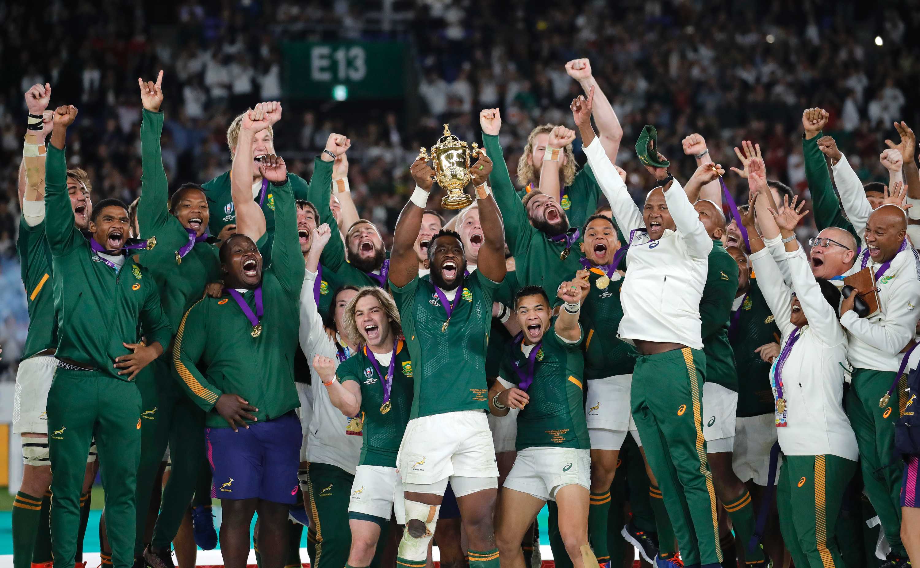 South African rugby union players celebrate with the Webb Ellis Cup on a podium after beating England.
