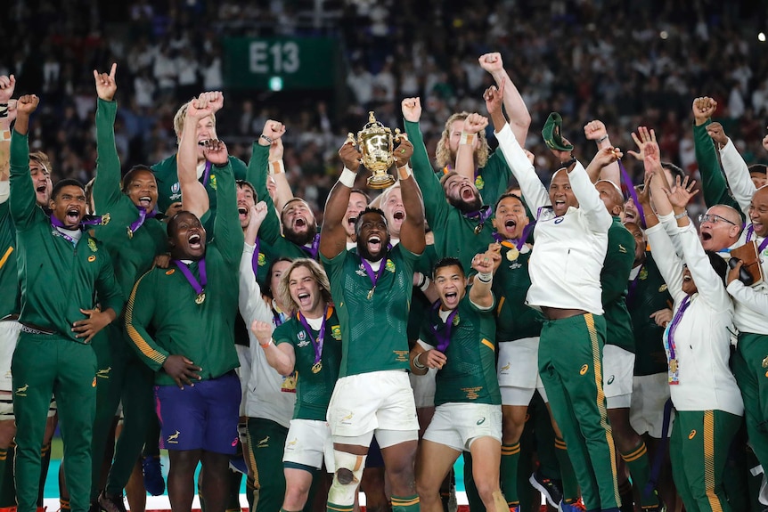 South African rugby union players celebrate with the Webb Ellis Cup on a podium after beating England.
