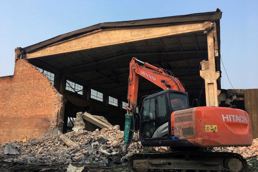 An excavator is seen on the debris in front of the demolished building.