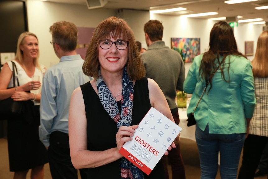 Sue Ellson holding up a copy of her book Gigsters at its launch in 2019