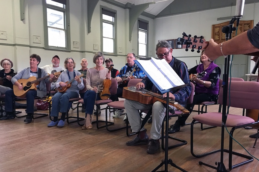 Girgarre locals playing guitars and violins at in a hall.