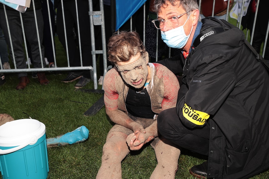 Guillaume Boivin, covered in mud, is attended to by a doctor as he holds sits and holds his wrist