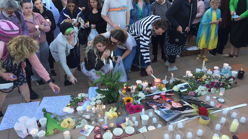 People lighting candles and laying down flowers at a flight of steps and crying.