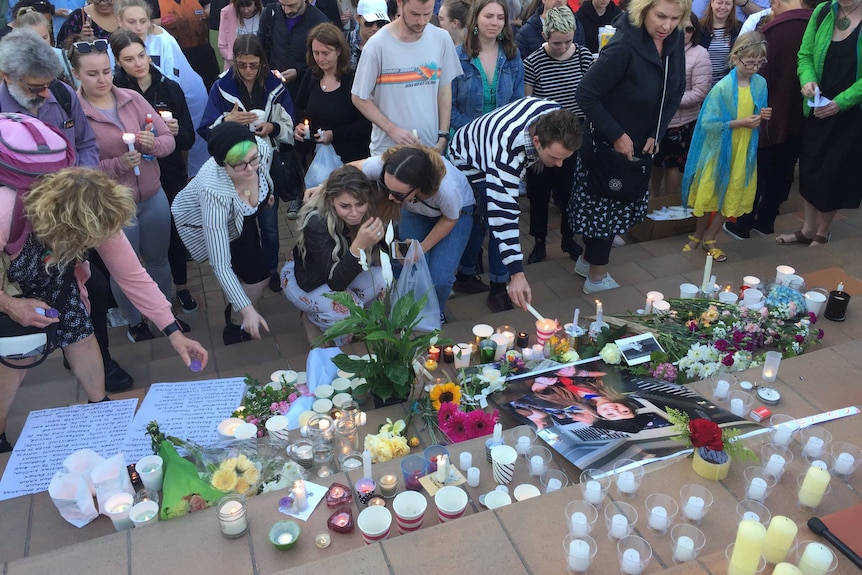 People lighting candles and laying down flowers at a flight of steps and crying.