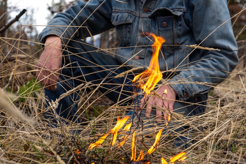 Male seated in dry grass with small fire in foreground