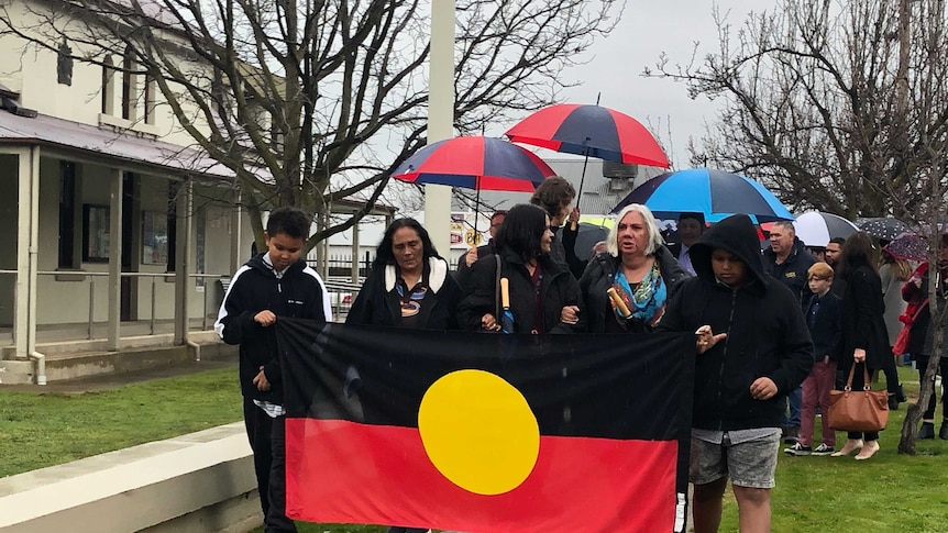 Friends and family holding a large Aboriginal flag walking down the street together
