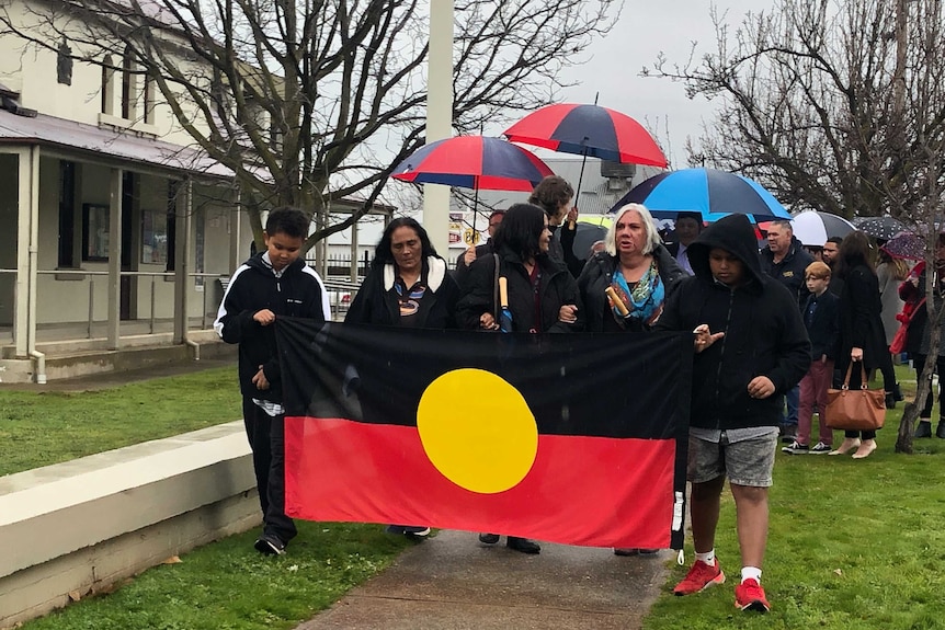 Friends and family of Naomi Williams holding Aboriginal flag walking down the street