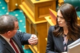 Grant Robertson gestures while talking to Jacinda Ardern. Both are carrying folders in their arms