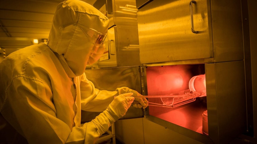 A scientist in a hazmat suit and mask puts silicon into a furnace for use in creating quantum chips