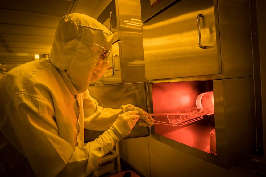 A scientist in a hazmat suit and mask puts silicon into a furnace for use in creating quantum chips