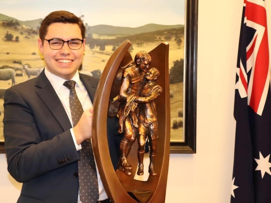 Bruce Lehrmann holds a trophy, standing next to an Australian flag in an office within Parliament House.
