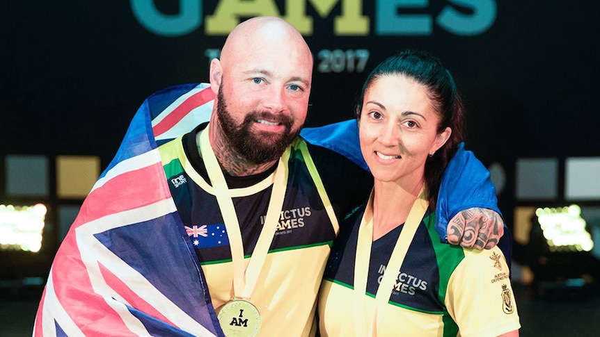Invictus Games athlete Tyrone Gawthorne wears a medal with an Australian flag over his shoulders, posing with a female athlete.