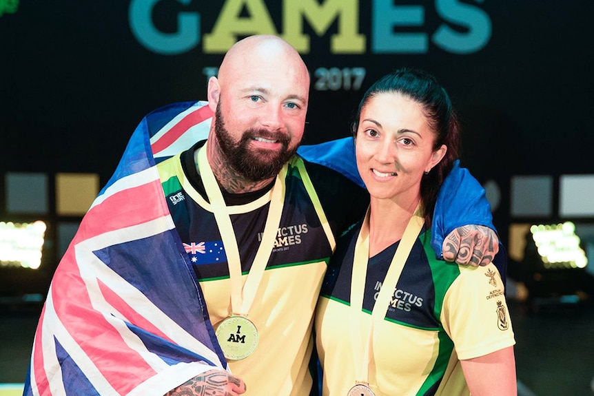 Invictus Games athlete Tyrone Gawthorne wears a medal with an Australian flag over his shoulders, posing with a female athlete.