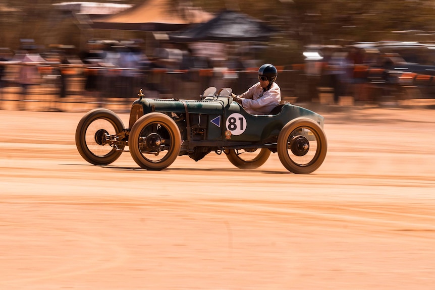 A vintage car races on a muddy track.  