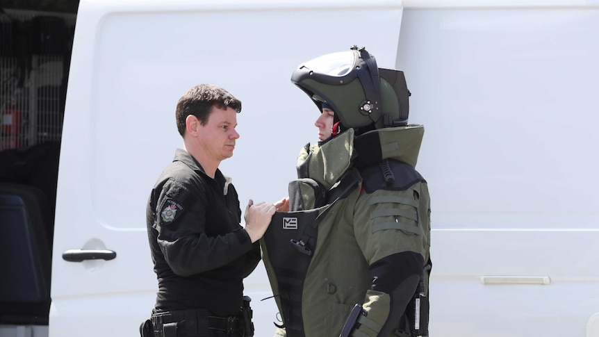 A uniformed police officer stands with a man in a protective suit and helmet.