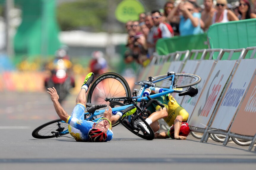 Two male para cyclists are on the ground after a crash in a road race.