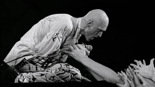 pete garrett of midnight oil holds a microphone as he is on his knees on stage looking at crowd