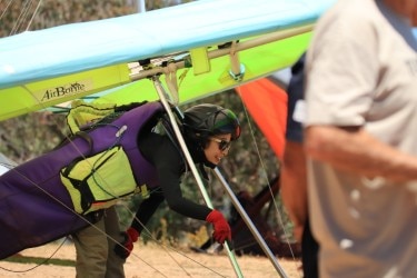 Uma asa delta feminina se apoia em seu planador no chão.
