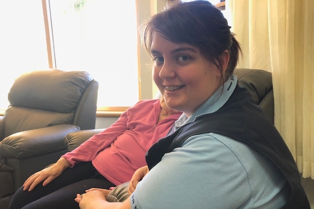 Aged care worker Carly Thompson, holding the hand of a resident, who is obscured.