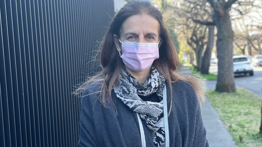 A woman in a pink surgical mask standing on a footpath