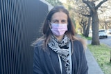 A woman in a pink surgical mask standing on a footpath