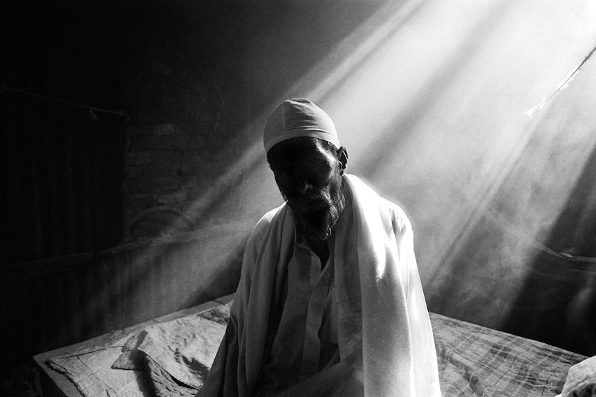 Light streams through a window onto the back of an old Bangladeshi man.