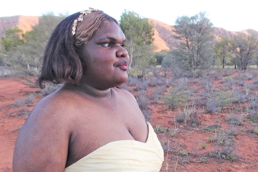 Young indigenous woman in strapless formal dress poses in desert landscape for fashion magazine