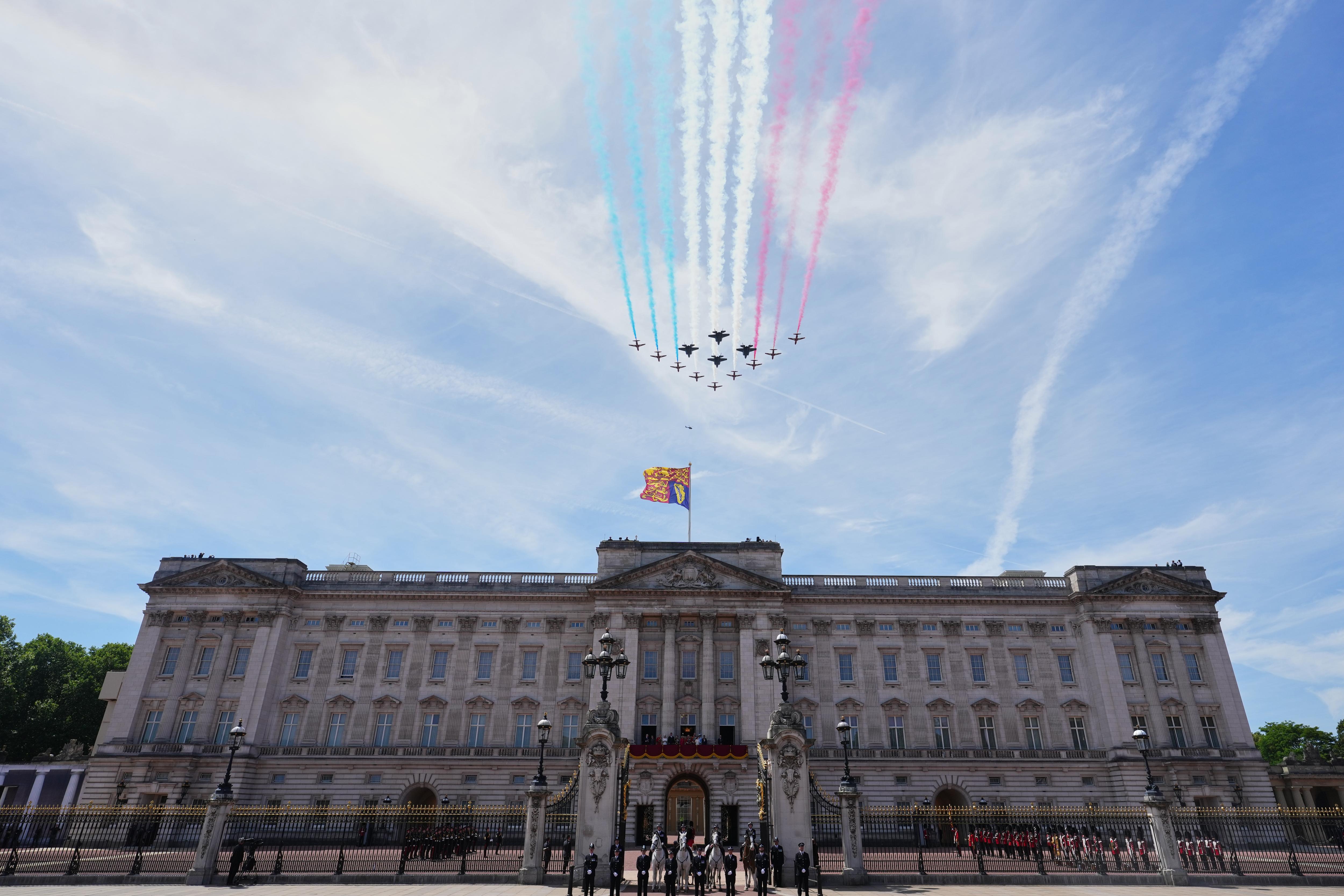 Jets fly over a palace in a clear blue sky leaving a trail of red, white and blue smoke behind them.