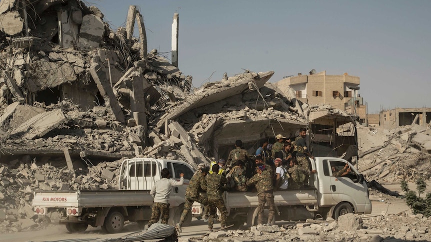 People wearing fatigues loaded into the back of a white truck survey large piles of debris.