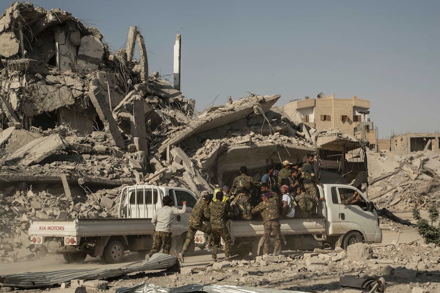 People wearing fatigues loaded into the back of a white truck survey large piles of debris.