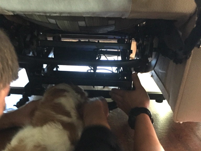 A puppy's head is stuck in the mechanics of a recliner chair.