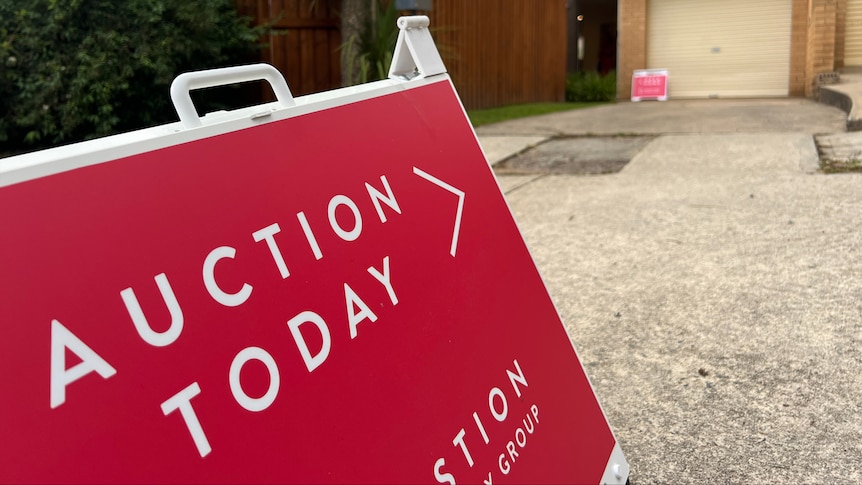 An A-frame sign that reads "auction today", directing toward a house.