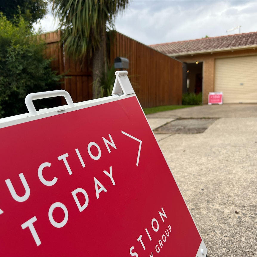 An A-frame sign that reads "auction today", directing toward a house.