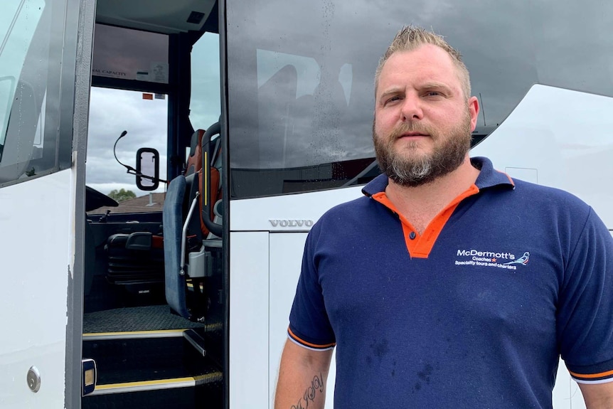 A man stands in front of a tour bus.