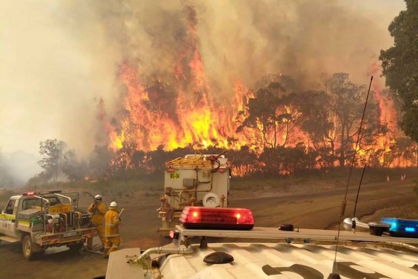A raging bushfire consumes bushland as fire crews watch on.