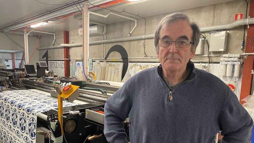 Man with greying hair wearing glasses and a sweater standing in front of printing machine in factory