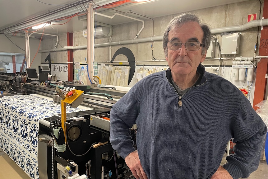 Man with greying hair wearing glasses and a sweater standing in front of printing machine in factory