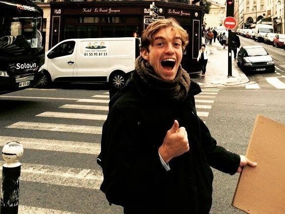 Man walking across the road on a crossing, smiling with thumbs up and holding cardboard.