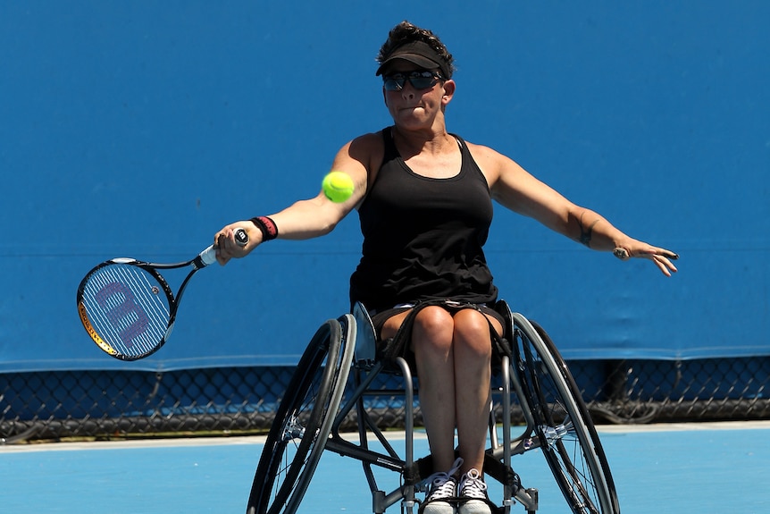 A wheelchair tennis player hits the ball with her racket