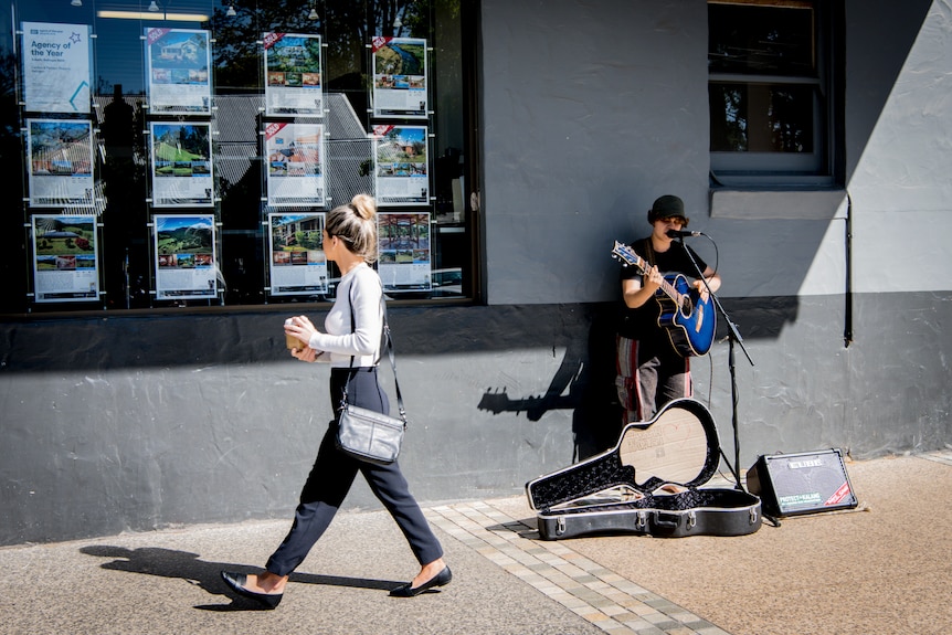 Woman walks past real office and busker plays