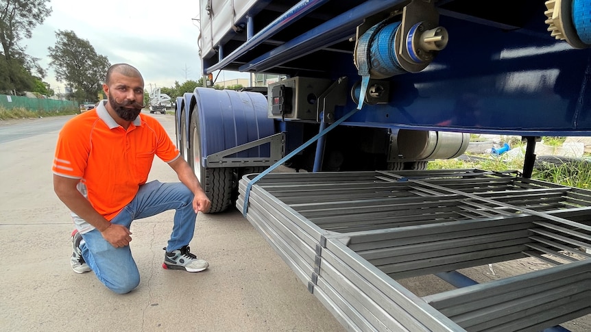 A man kneels down in front of a truck trailer.