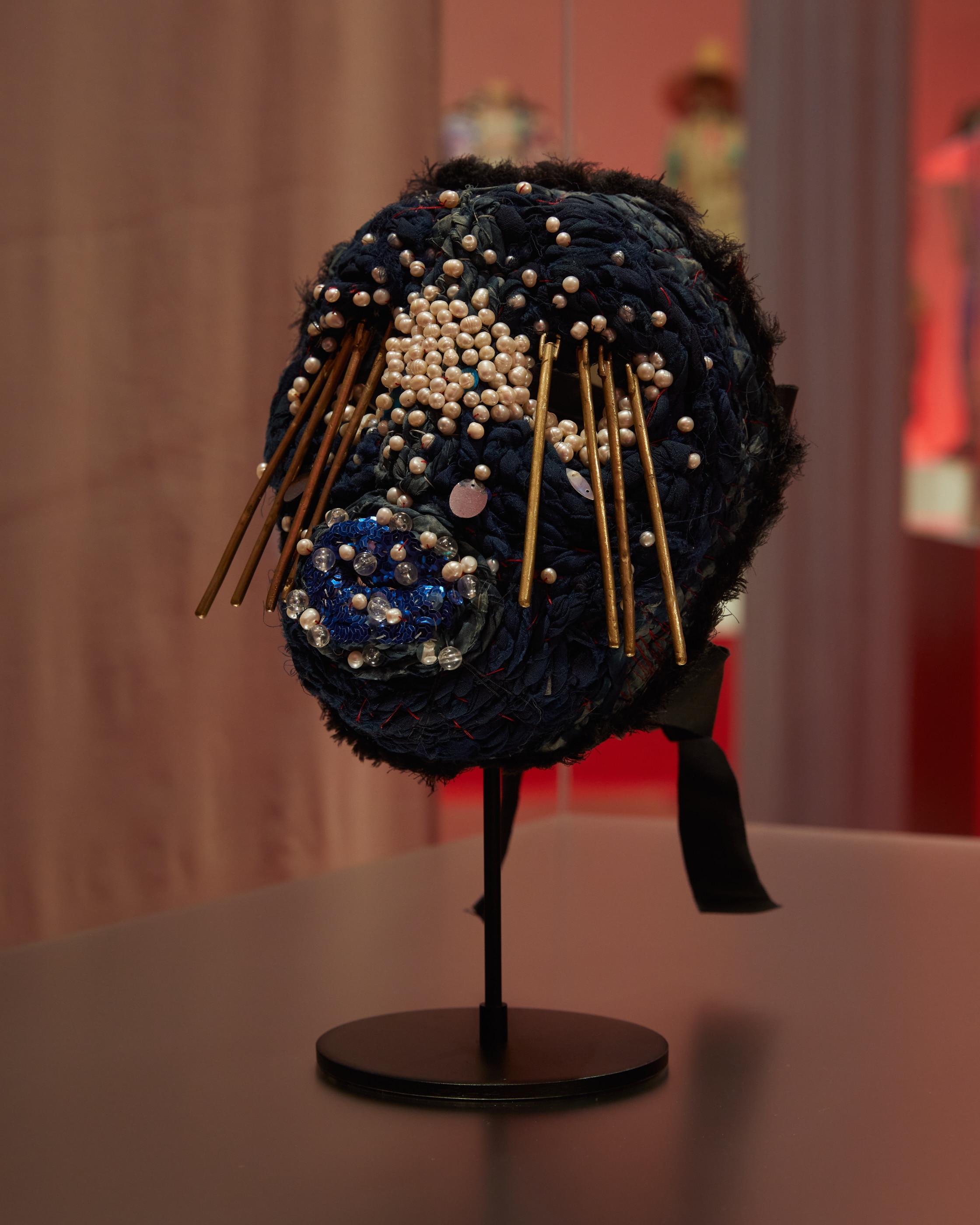 A mannequin with a mask attached with indigo knitwear as the base, pearls concentrated in the centre, sticks as eyelashes. 