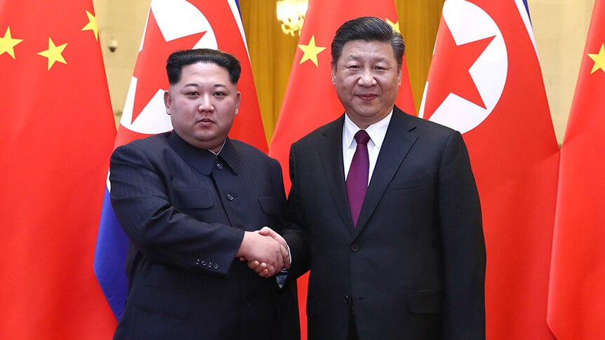 Kim Jong-un shakes hands with Xi Jinping in front of North Korean and Chinese flags.