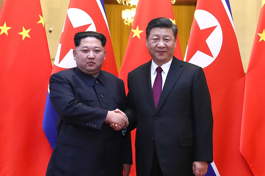 Kim Jong-un shakes hands with Xi Jinping in front of North Korean and Chinese flags.