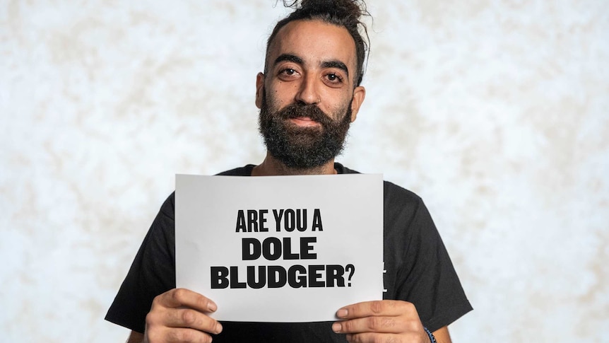 Nickolas Koutsoudakis is holding a sign that reads "Are you a dole bludger?"