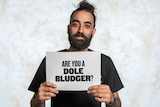 Nickolas Koutsoudakis is holding a sign that reads "Are you a dole bludger?"