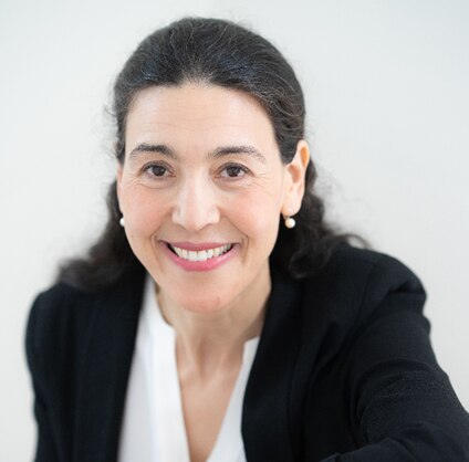 A professional looking woman wearing a suit and pearl earrings.