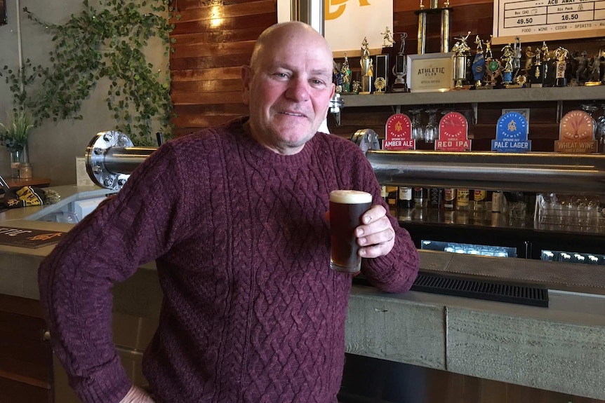 Man stands at bar holding a glass of dark  beer